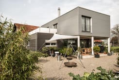Modernes Einfamilienhaus mit Metallfassade, grosser Terrasse und Gartenbereich an sonnigem Tag.