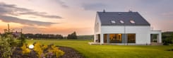 Modernes Einfamilienhaus mit Garten bei Sonnenuntergang, Architektur mit großen Fenstern und gepflegtem Rasen.